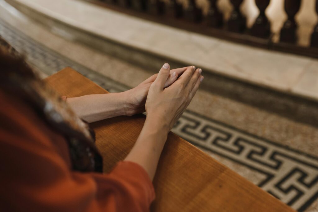 A close-up image of hands together in prayer on a wooden surface in an indoor setting.